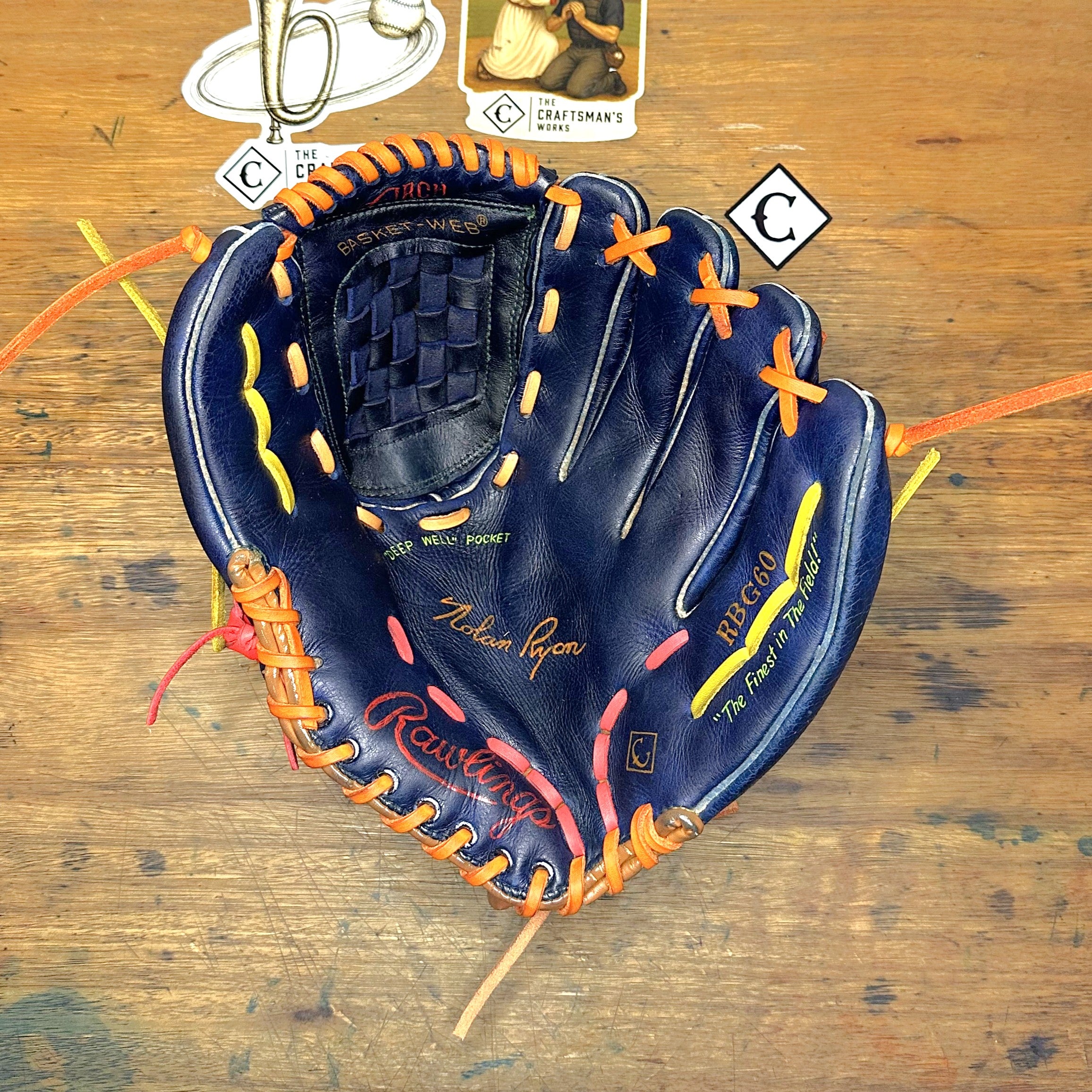 The Tequila Sunrise Nolan Ryan RBG60 glove laying on a desk with the palm side facing up.