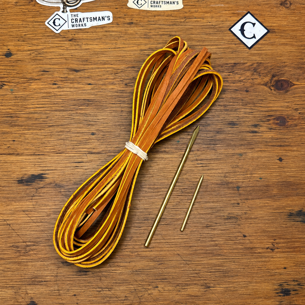 Tan premium quality glove laces with two brass perma-loc lacing needles sitting on a wooden dest.