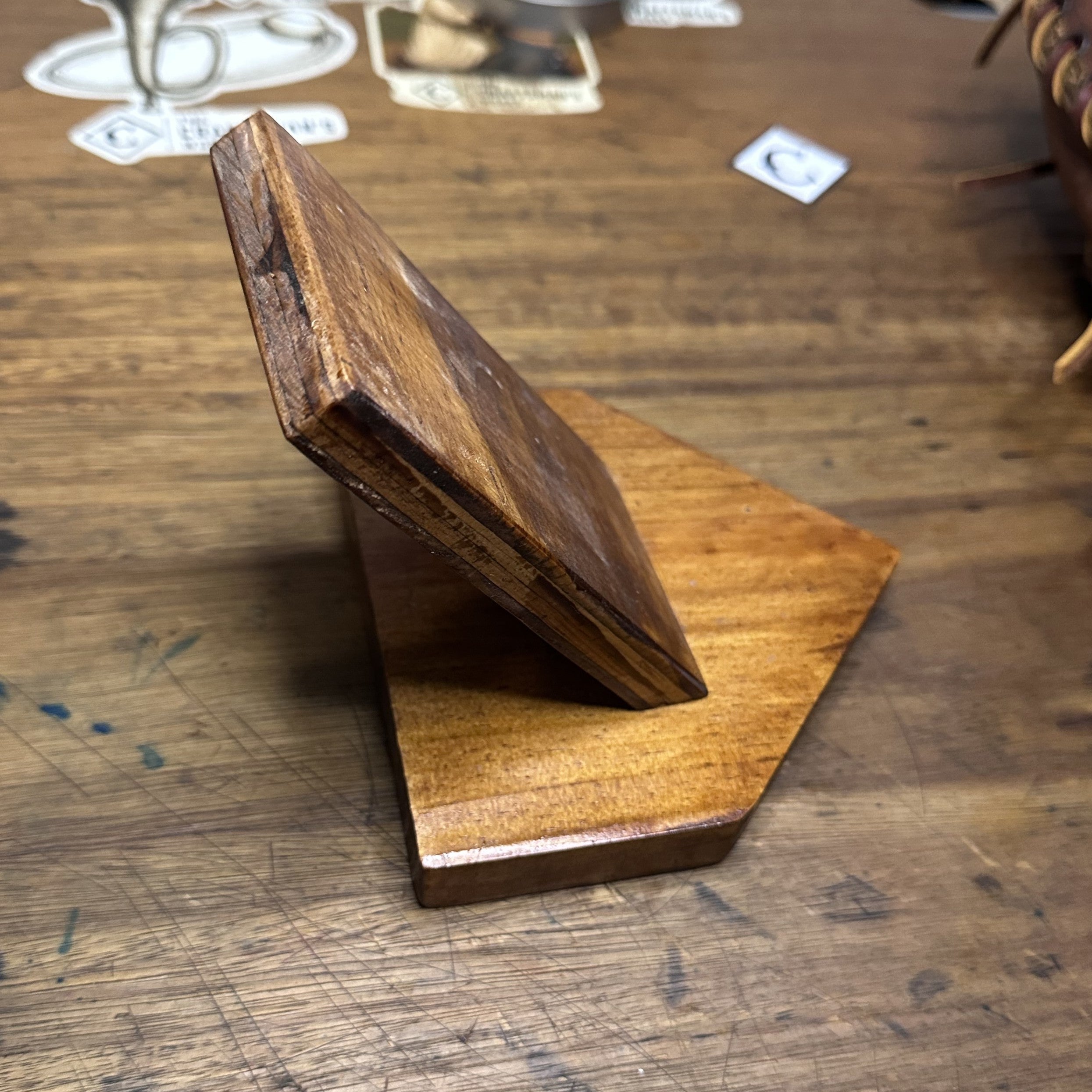 A small wooden baseball glove display stand made of two wooden pieces, one leaning against the other on a rustic wooden tabletop.
