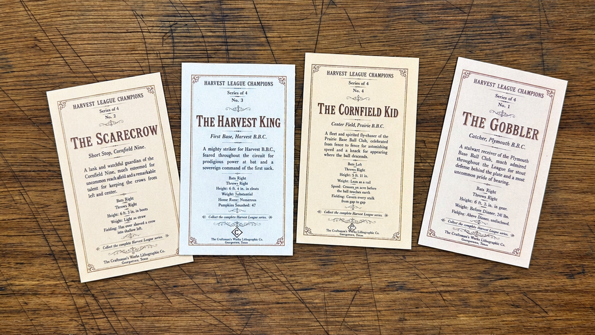 Four vintage-style printed cards or labels laid out on a worn wooden tabletop. The cards have aged cream and off-white backgrounds with decorative borders and text including 'Harvest League Champions' and titles such as The Scarecrow, The Harvest King, The Cornfield Kid, and The Gobbler.