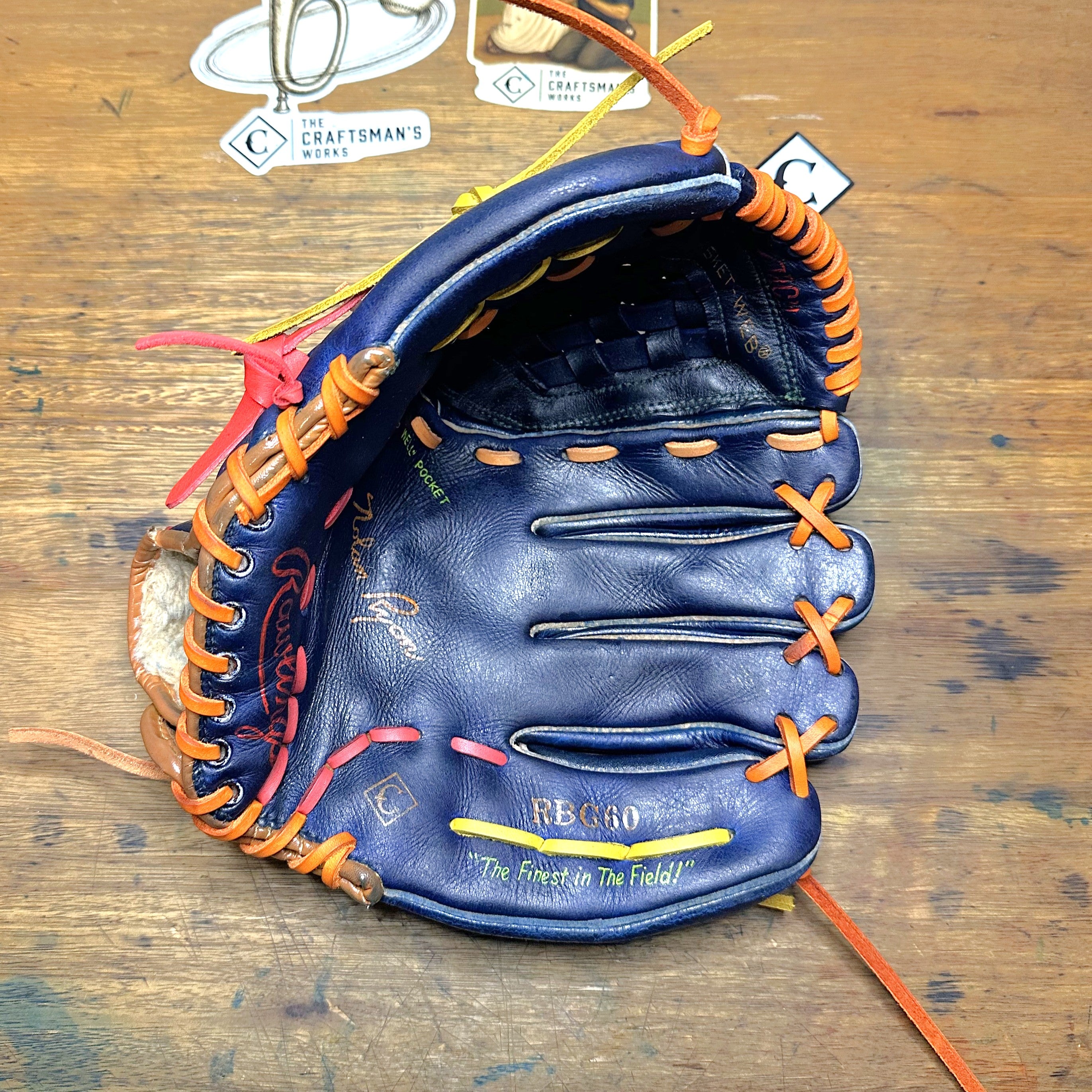 The Tequila Sunrise Nolan Ryan RBG60 glove laying on a desk with the palm side facing up.