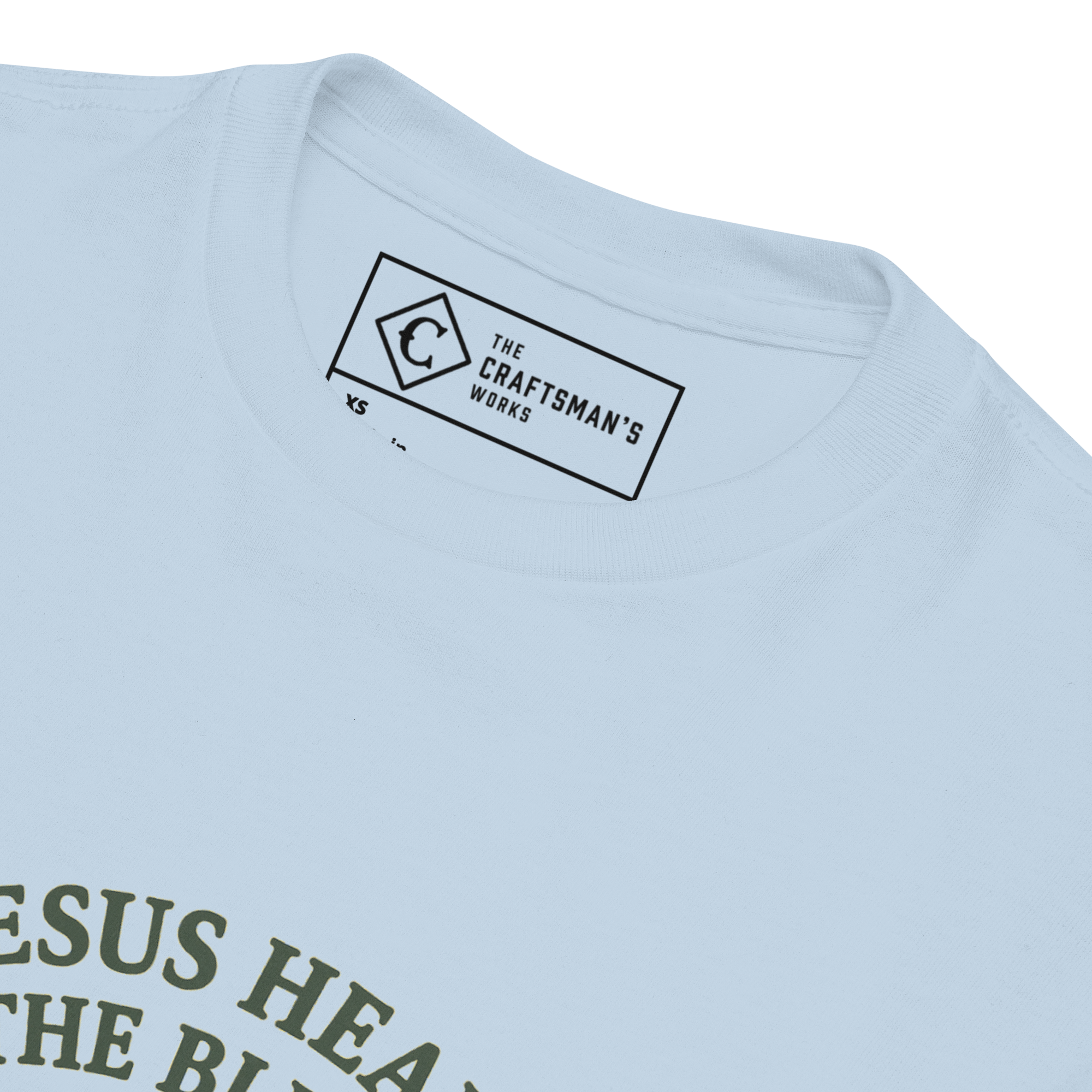 Close-up of a light blue crewneck t-shirt showing the inner neck label which reads 'THE CRAFTSMAN'S WORKS' and part of a dark olive green graphic print on the lower left.